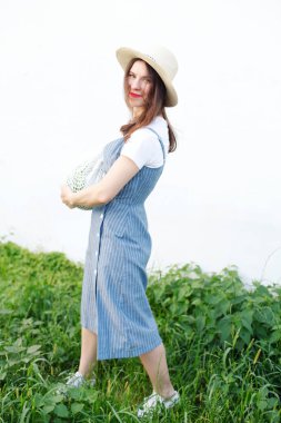 Şapkalı genç kadın, örgü çantada karpuzla poz veren denim elbise