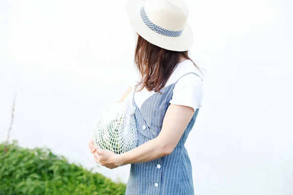 Pretty woman carrying watermelon in knitted bag in yard