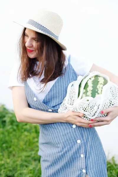 Young woman carrying watermelon in knitted bag