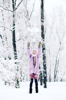 Genç mutlu kadın parkta karla oynuyor.