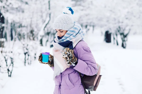 young woman holding reusable cup with warming drink in winter park