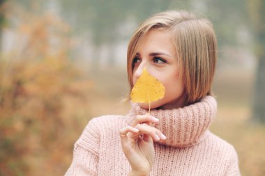 Sonbahar yaprağıyla parkta poz veren genç bir kadın.