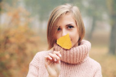 Sonbahar yaprağıyla parkta poz veren genç bir kadın.