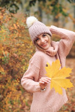 Sonbahar yaprağıyla parkta poz veren genç bir kadın.