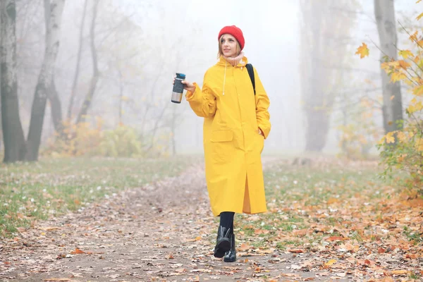 young woman in yellow raincoat posing in autumn park