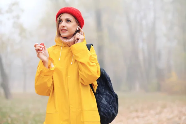 young woman in yellow raincoat using bluetooth earphones outdoors