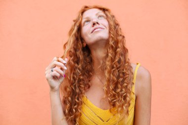 Uçan kıvırcık saçlı, turuncu arka planda kameraya gülen güzel kızıl saçlı kızın portresi..