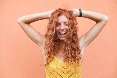 Uçan kıvırcık saçlı, turuncu arka planda kameraya gülen güzel kızıl saçlı kızın portresi..