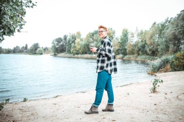 Nehir kıyısında duran güneş gözlüklü ve kot ceketli genç adam.