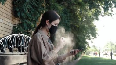 Sokakta cep telefonu spreyiyle dezenfekte eden bir kız.