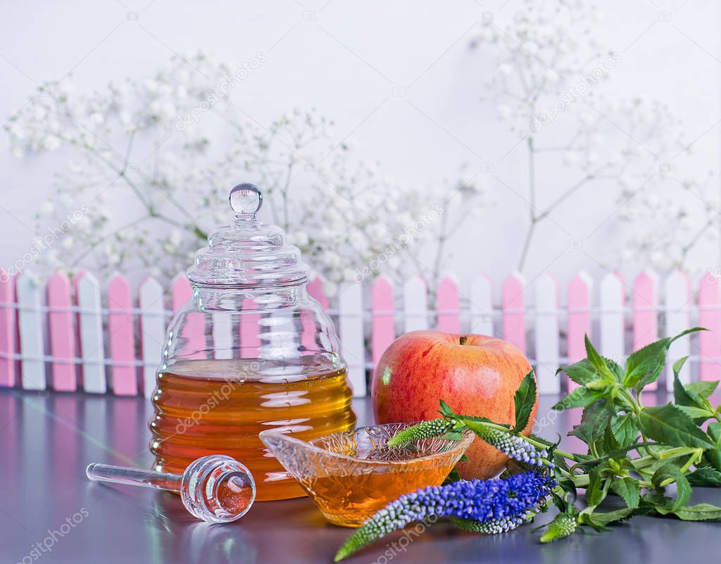 Rosh Hashanah Jewish holiday concept - red yellow apple, glass dipper, saucer, honey jar on grey table and white flowers. Traditional holiday symbols