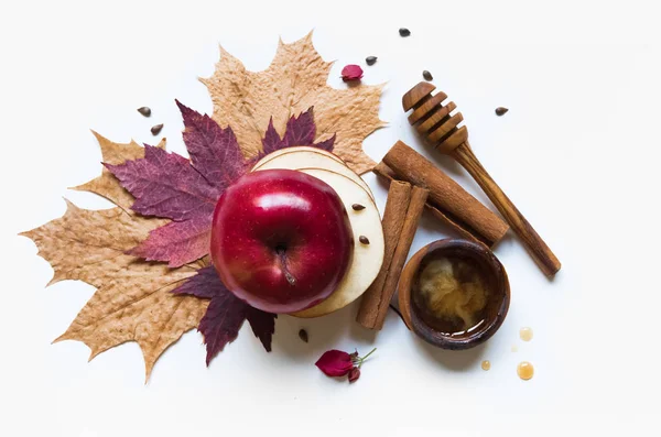 Rosh Hashanah Jewish holiday concept - red apple, wooden dipper, saucer of honey on autumn maple leaves, white background with pink flowers and cinnamon. Traditional holiday symbols