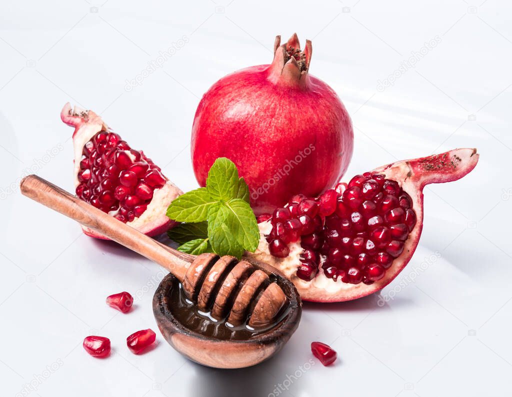 Rosh Hashanah Jewish holiday concept - red pomegranate and two slices, honey in wooden saucer with honey dipper. Traditional holiday symbols