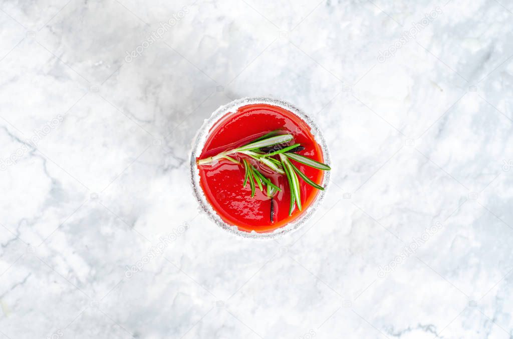 Tomato juice garnished with a rosemary branch on a marble background, with copy space