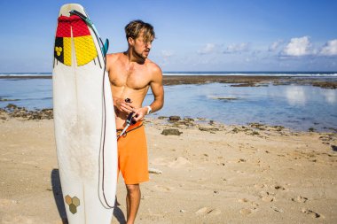 young man with surfing board on sandy beach near ocean clipart
