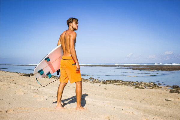 young surfer with surfing board standing on sandy beach on summer day