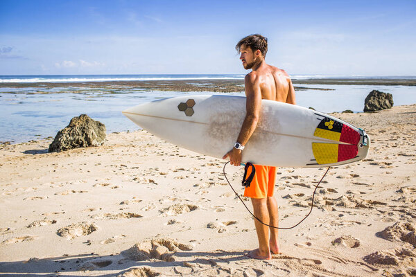 side view of young surfer with surfing board standing on sandy beach on summer day