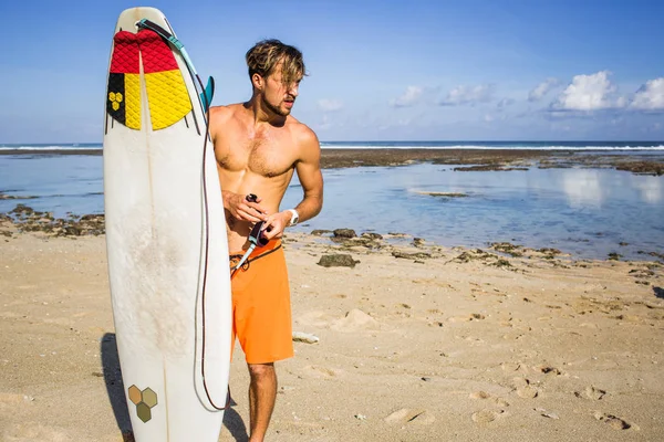 young man with surfing board on sandy beach near ocean