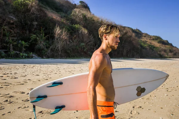 side view of man with surfing board looking away on sandy beach