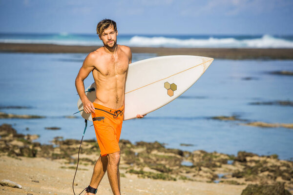 surfer with surfing board running on sandy beach on summer day