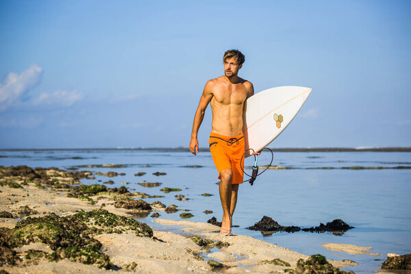 young sportsman with surfing board walking on sandy beach 
