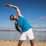 Sportman in zonnebril uitrekken op strand in de buurt van de zee