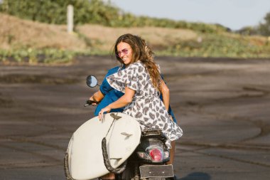 Bali, Endonezya kumsalda arkadan görünüşü çift sürme scooter surfboard ile
