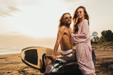 gün batımı sırasında çift ayakta Bali, Endonezya-yakınındaki plajda surfboard ile scooter gülümseyen