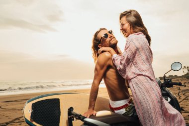 scooter üzerinde bali, Endonezya beach yakınındaki çift ayakta gülüyor