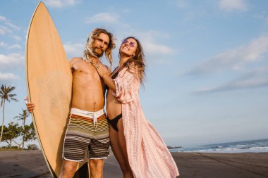 yakışıklı sörfçü Bali, Endonezya kumsalda gülümseyen kız ve holding sörf tahtası sarılma