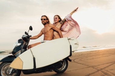 Bali, Endonezya kumsalda surfboard ile motosiklet sürme çift