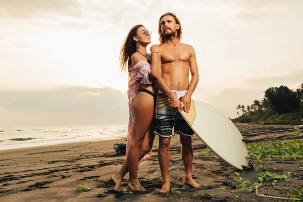 Lächelnde Freundin Umarmt Freund Mit Surfbrett Strand Bei Sonnenuntergang Bali — kostenloses Stockfoto