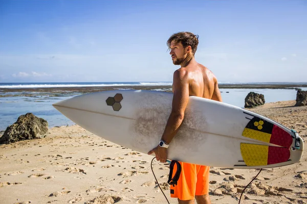 Vista lateral do jovem surfista com prancha de surf em pé na praia de areia no dia de verão — Fotografia de Stock