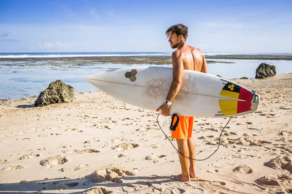 Side view of young surfer with surfing board standing on sandy beach on summer day — Stock Photo