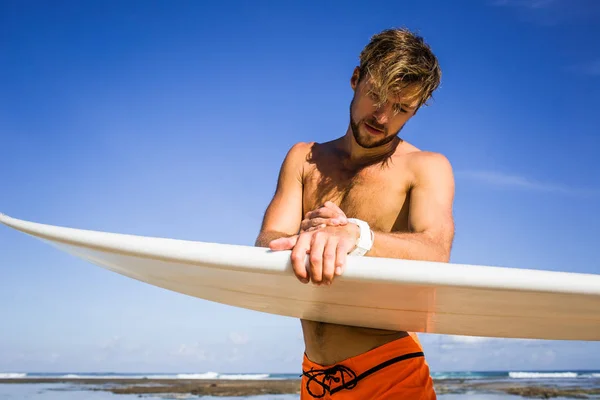 Athletic sportsman with surfing board checking time on coastline on summer day — Stock Photo