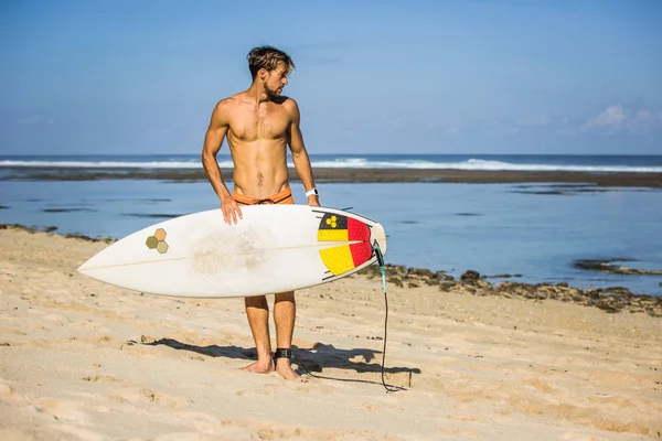 Young man with surfing board on sandy beach near ocean — Stock Photo