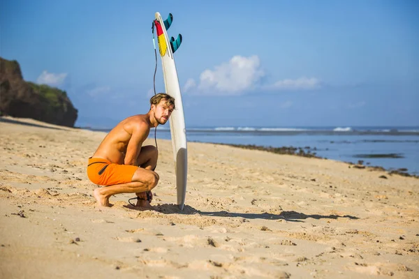 Young man with surfing board on sandy beach near ocean — Stock Photo