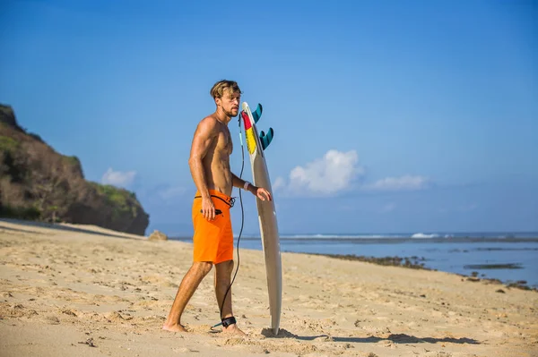 Vista lateral del joven con tabla de surf en la playa de arena cerca del océano - foto de stock