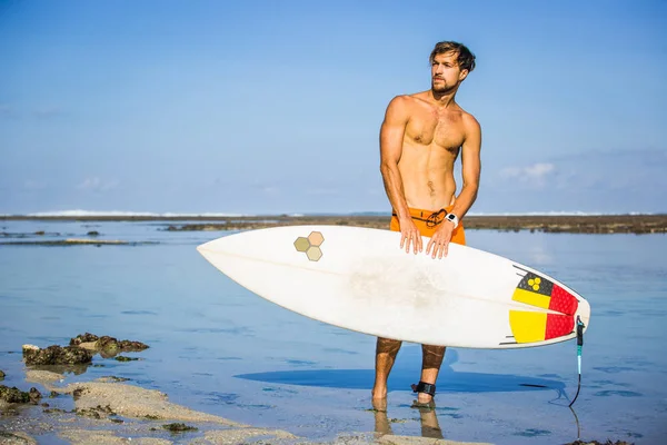 Deportista atlético con tabla de surf mirando hacia fuera en la costa en el día de verano - foto de stock