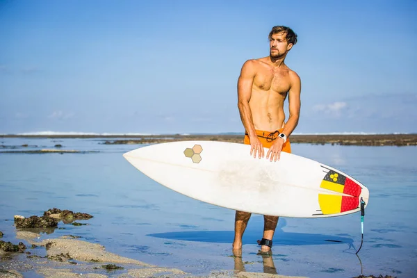 Athletic sportsman with surfing board looking away on coastline on summer day — Stock Photo