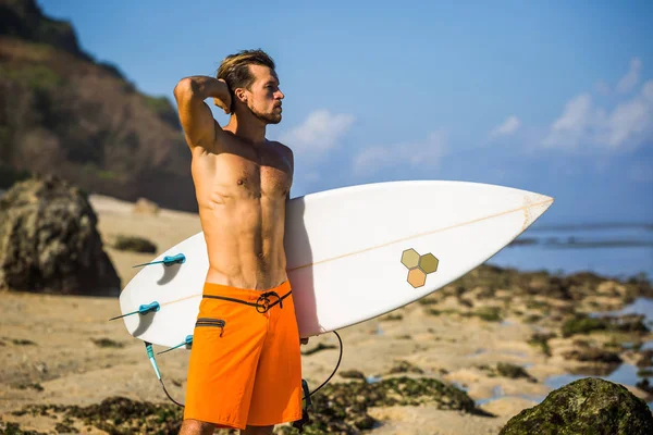 Young surfer with surfing board standing on sandy beach near ocean — Stock Photo