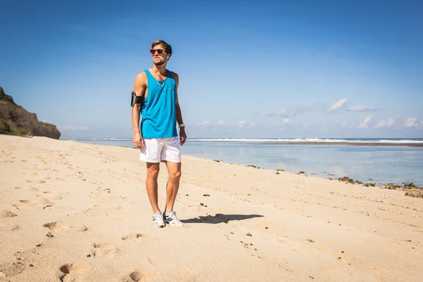 Deportista en gafas de sol con brazalete caminando por la playa, Bali, Indonesia - foto de stock