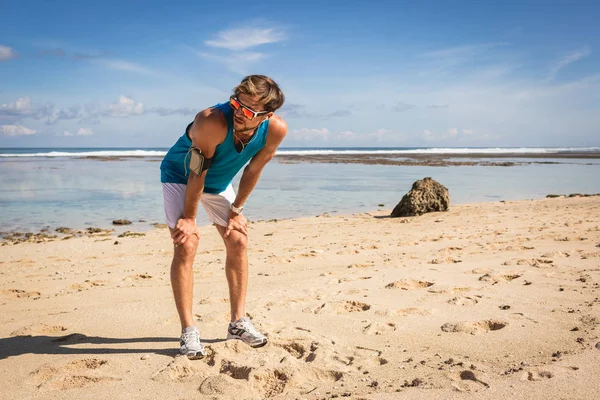 Deportista cansado de pie y descansando en la playa - foto de stock