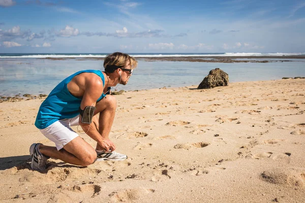 Sportsman tying shoelaces on sneakers on beach near sea — Stock Photo