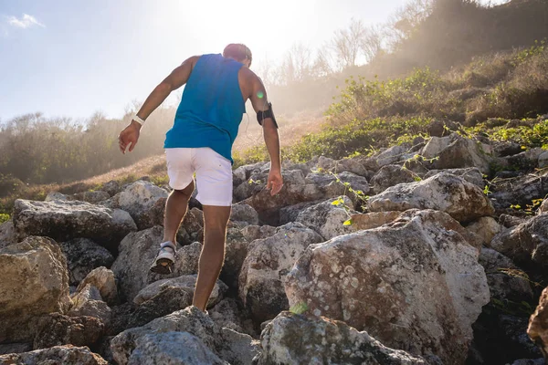 Back view of athletic man climbing on rocks on mountain with back light — Stock Photo
