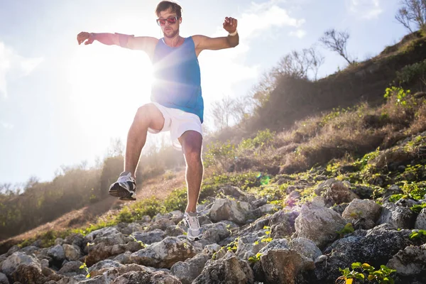 Bottom view of sportsman jumping from rocks with back light — Stock Photo