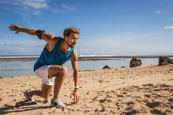 Hombre atlético con brazalete haciendo saltos durante el entrenamiento en la orilla del mar - foto de stock