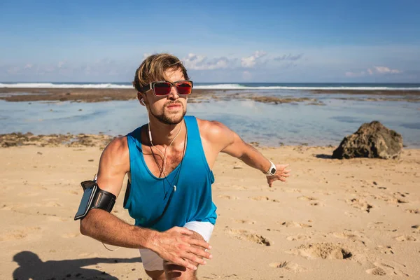 Deportista con brazalete de teléfono inteligente trabajando en la playa cerca del mar - foto de stock