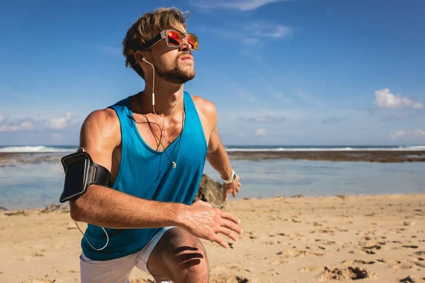 Sportivo che ascolta musica con bracciale smartphone mentre fa salti sulla spiaggia — Foto stock