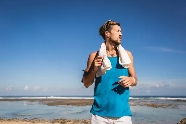 Uomo atletico in abbigliamento sportivo con asciugamano in piedi in mare — Foto stock